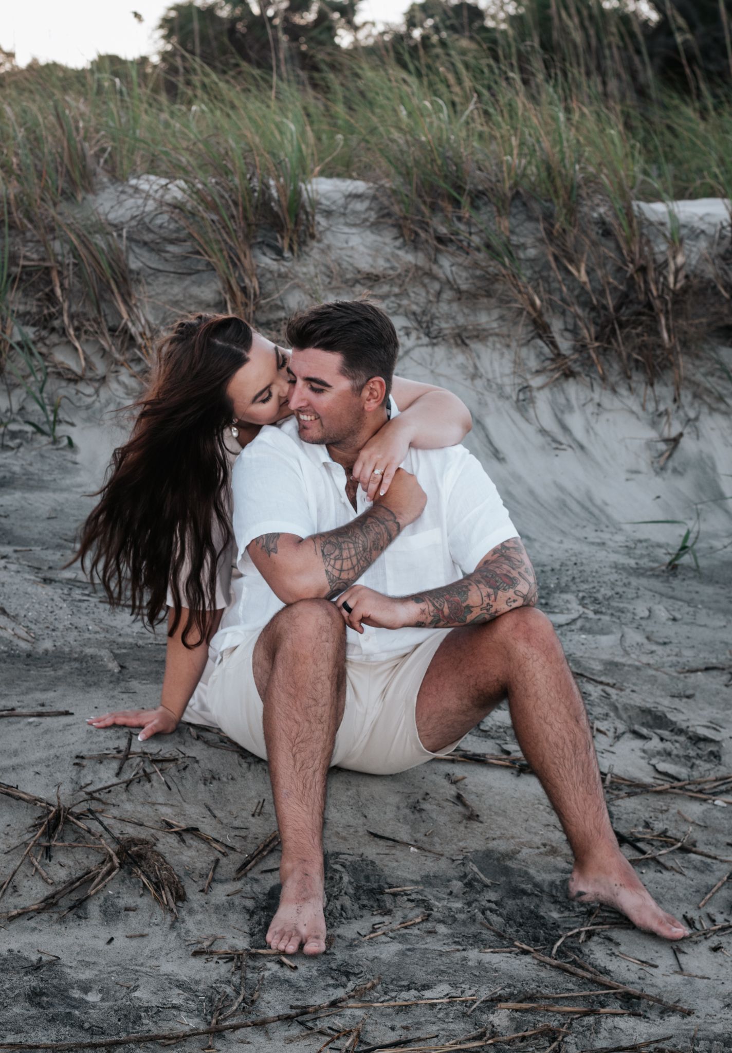 A couple sharing a romantic moment on sandy dunes during a beach photoshoot.