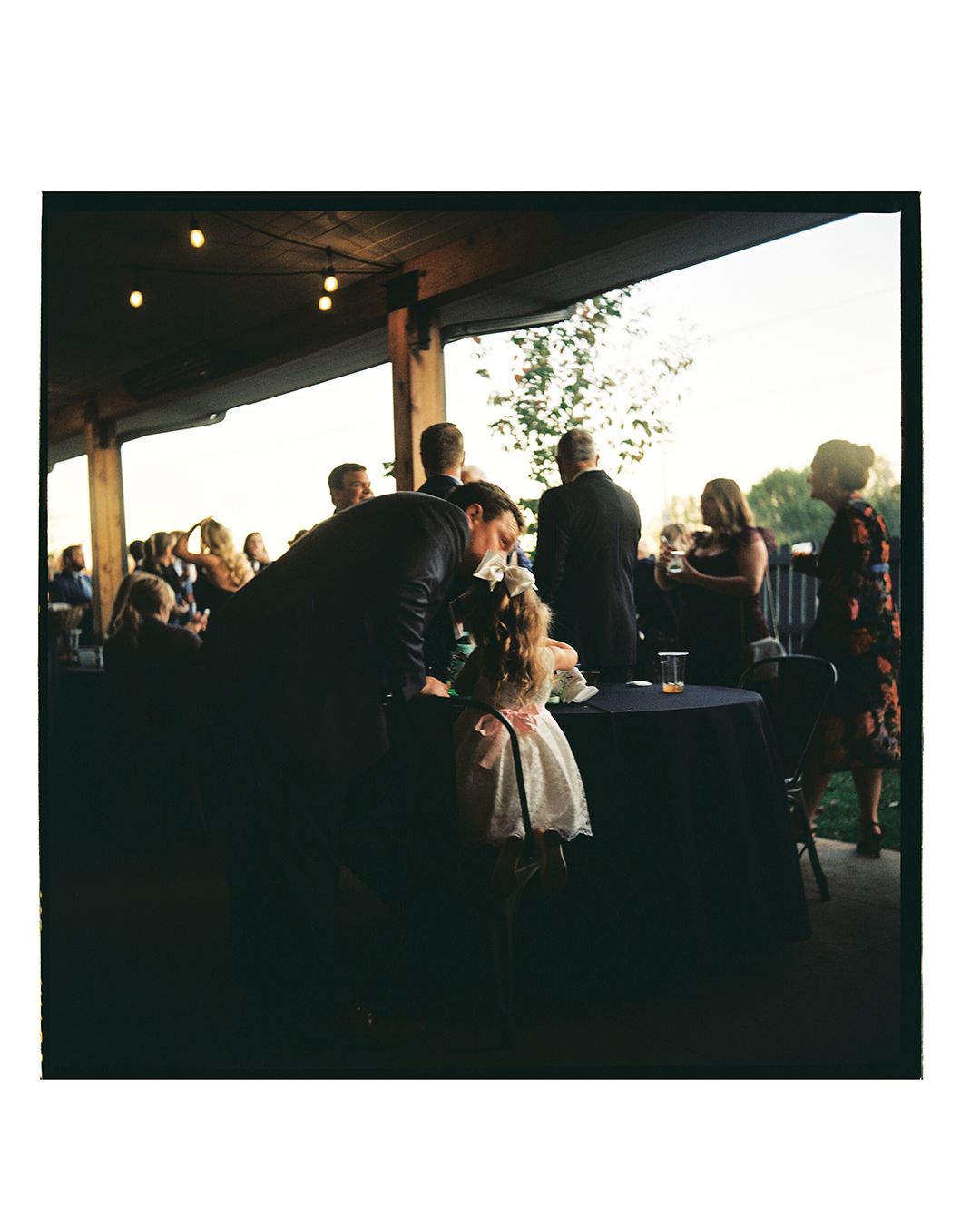 Wedding guests mingle during cocktail hour on a covered patio at dusk.