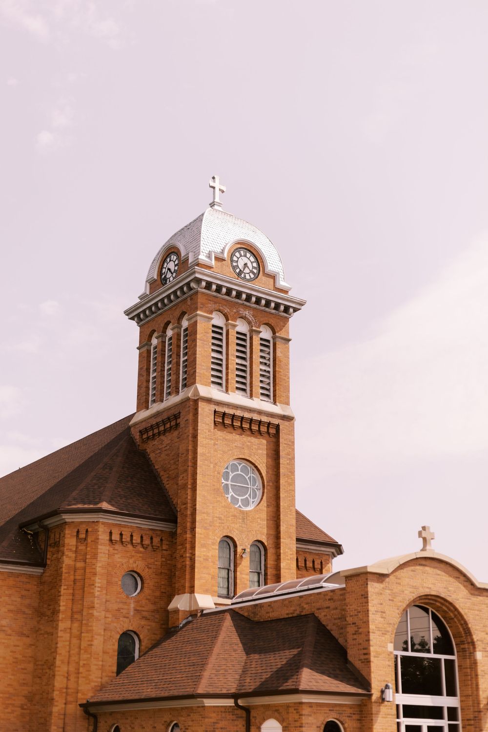 Brick church with clock tower and cross against cloudy sky.