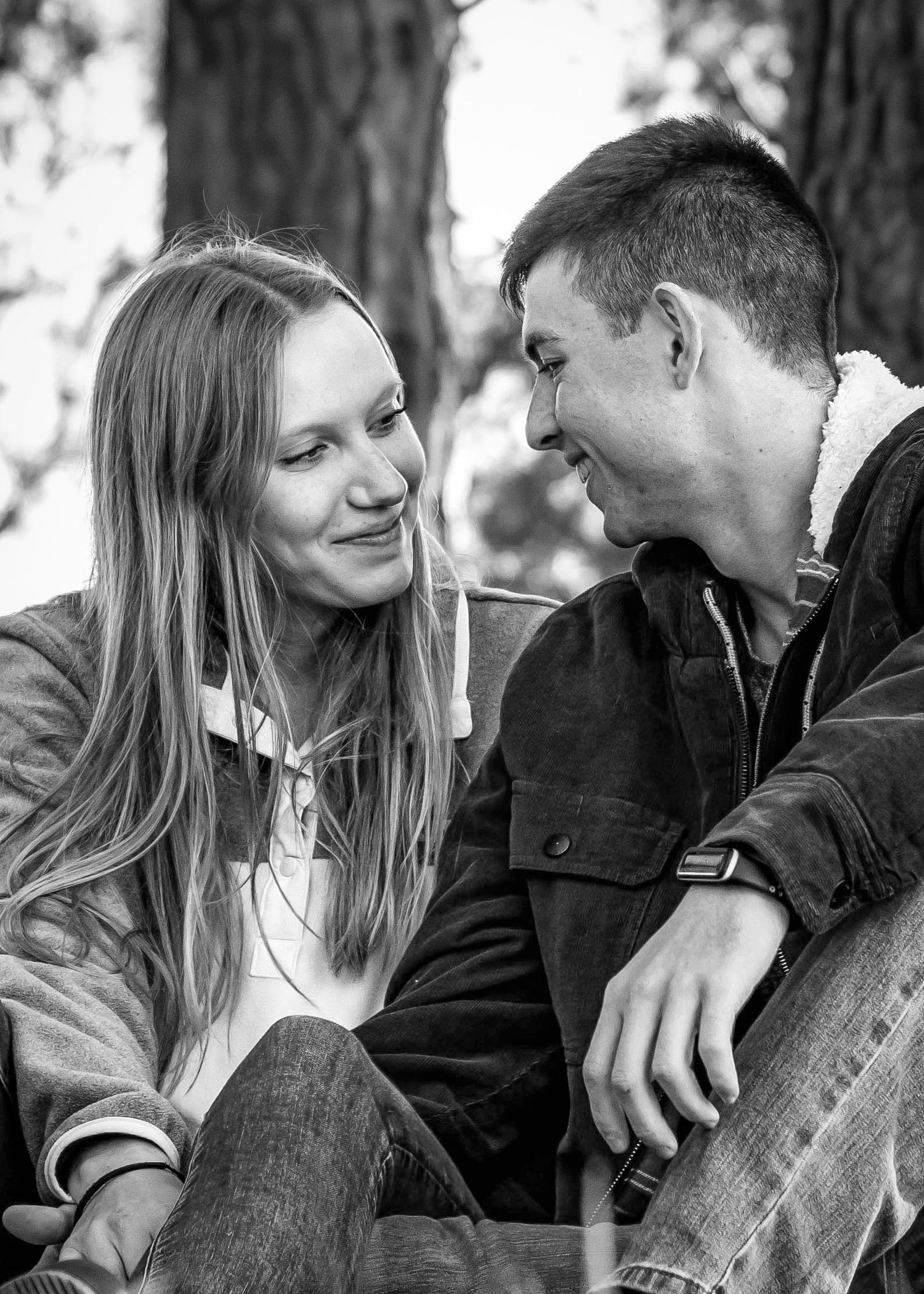 a man and woman look at each other while sitting under a tree. black and white