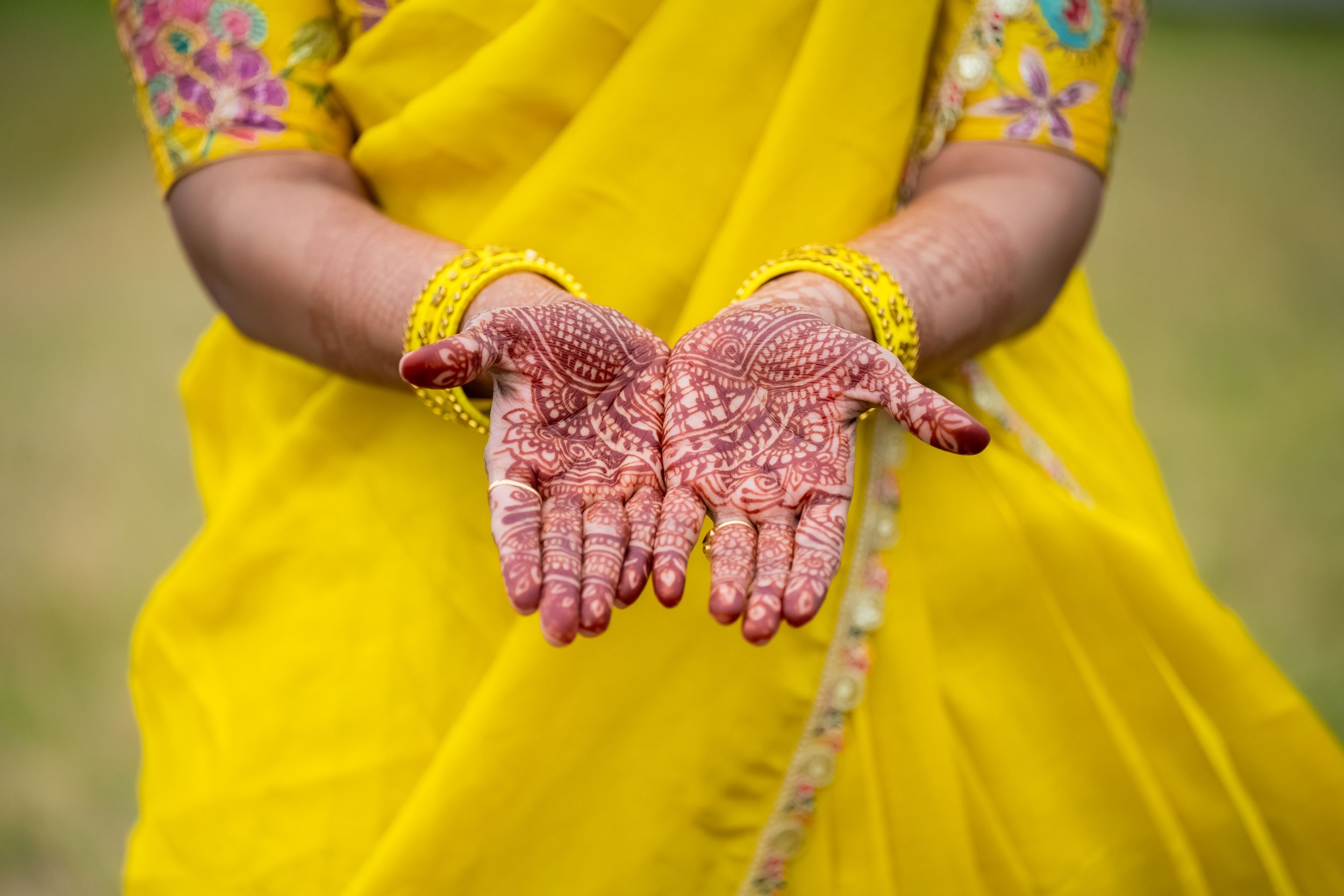 Woman in yellow sari displaying intricate henna mehndi designs on her palms at a traditional Indian wedding ceremony.