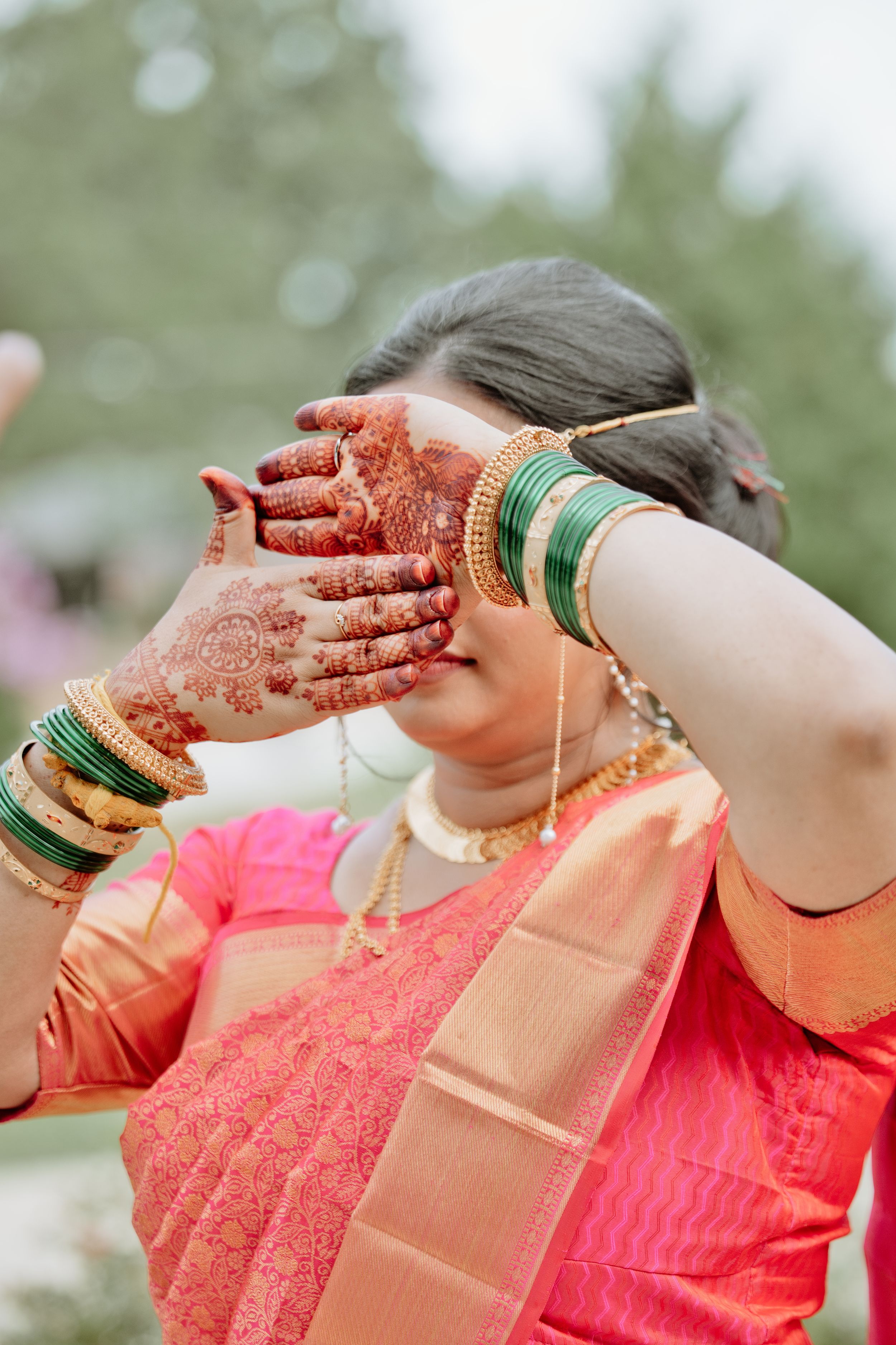 Indian bride in pink saree displaying intricate henna mehndi designs on hands, wearing gold and green bangles at wedding.