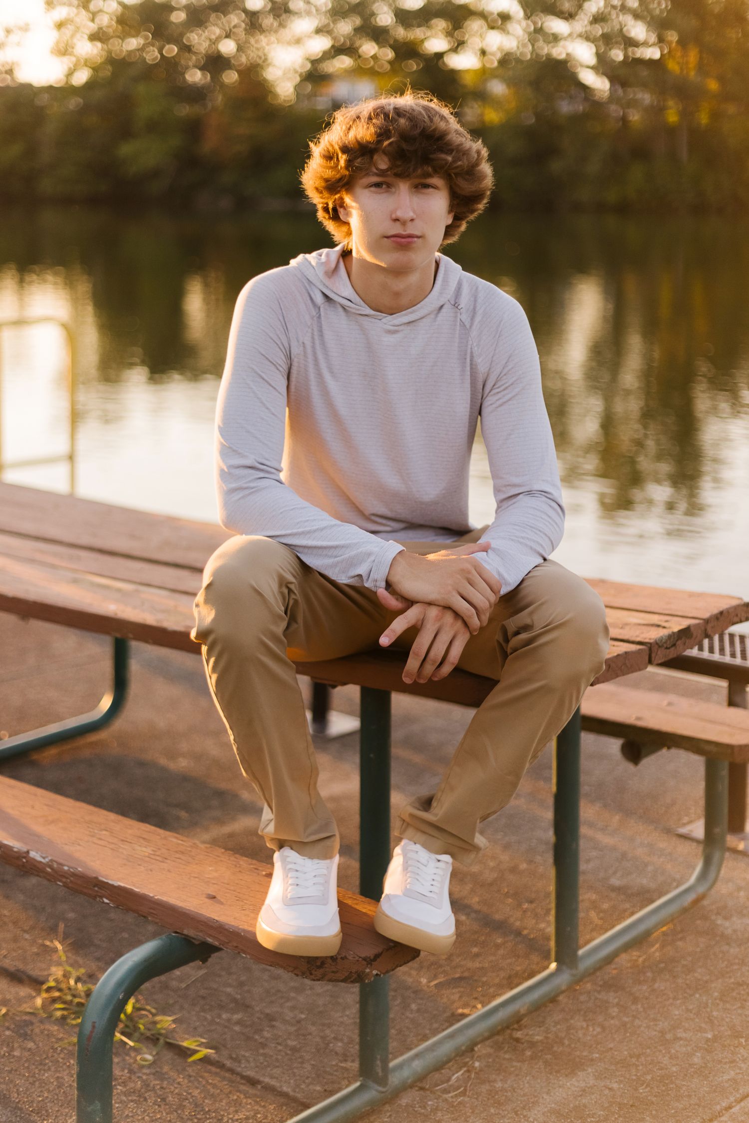 A sunset portrait of someone sitting on a picnic table wearing casual clothes near a lake.