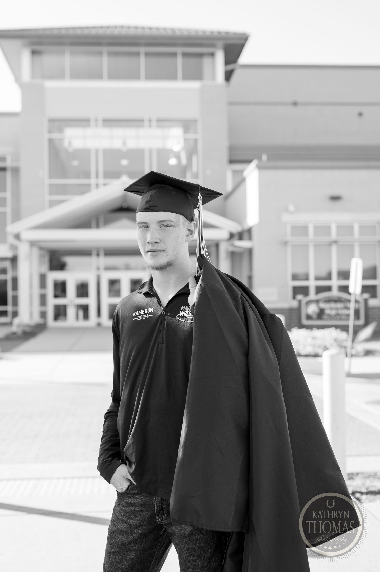 Black and white portrait of graduate in cap and gown against modern architecture.