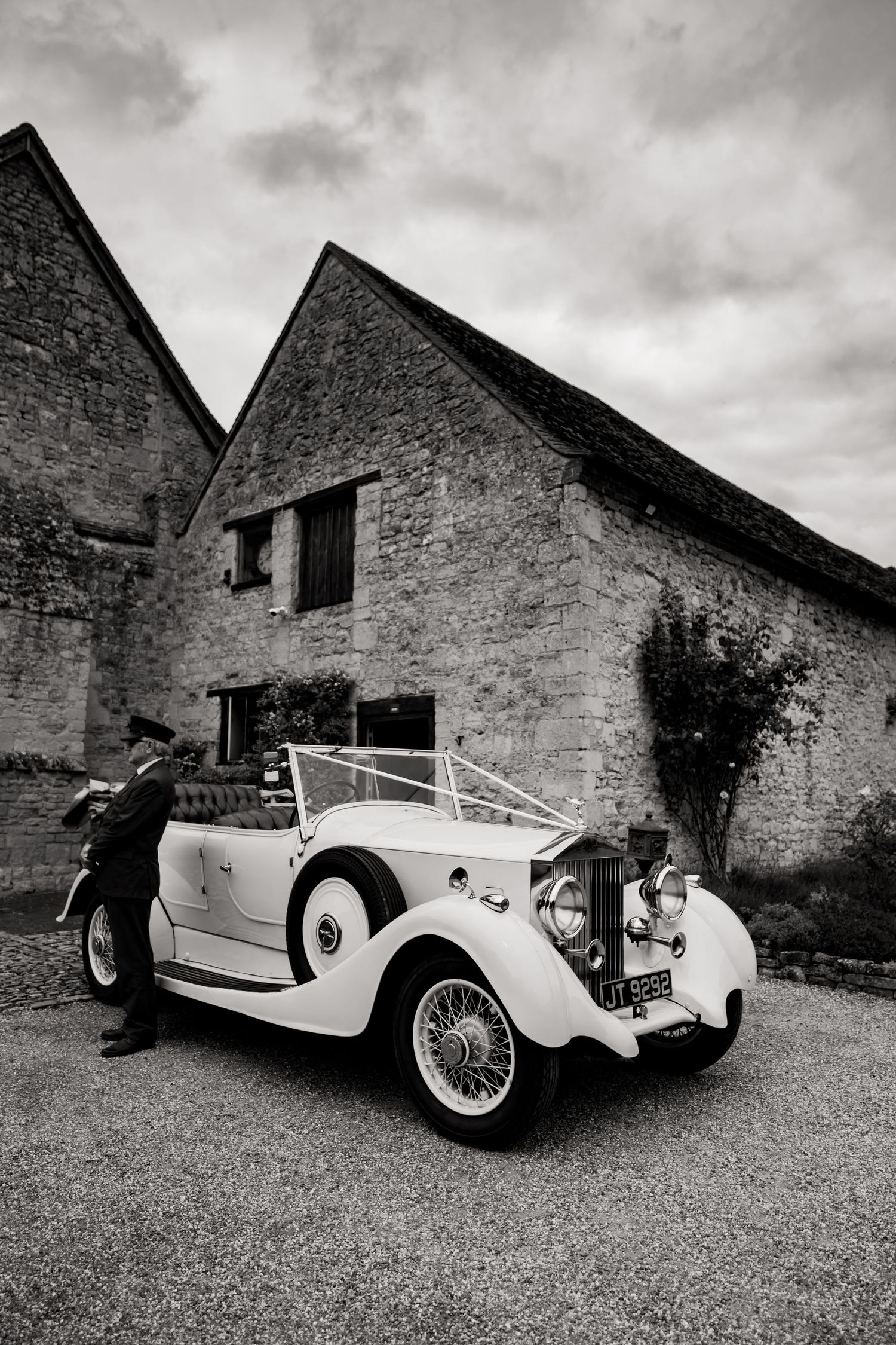 Vintage white luxury car parked outside rustic stone buildings in black and white photography.