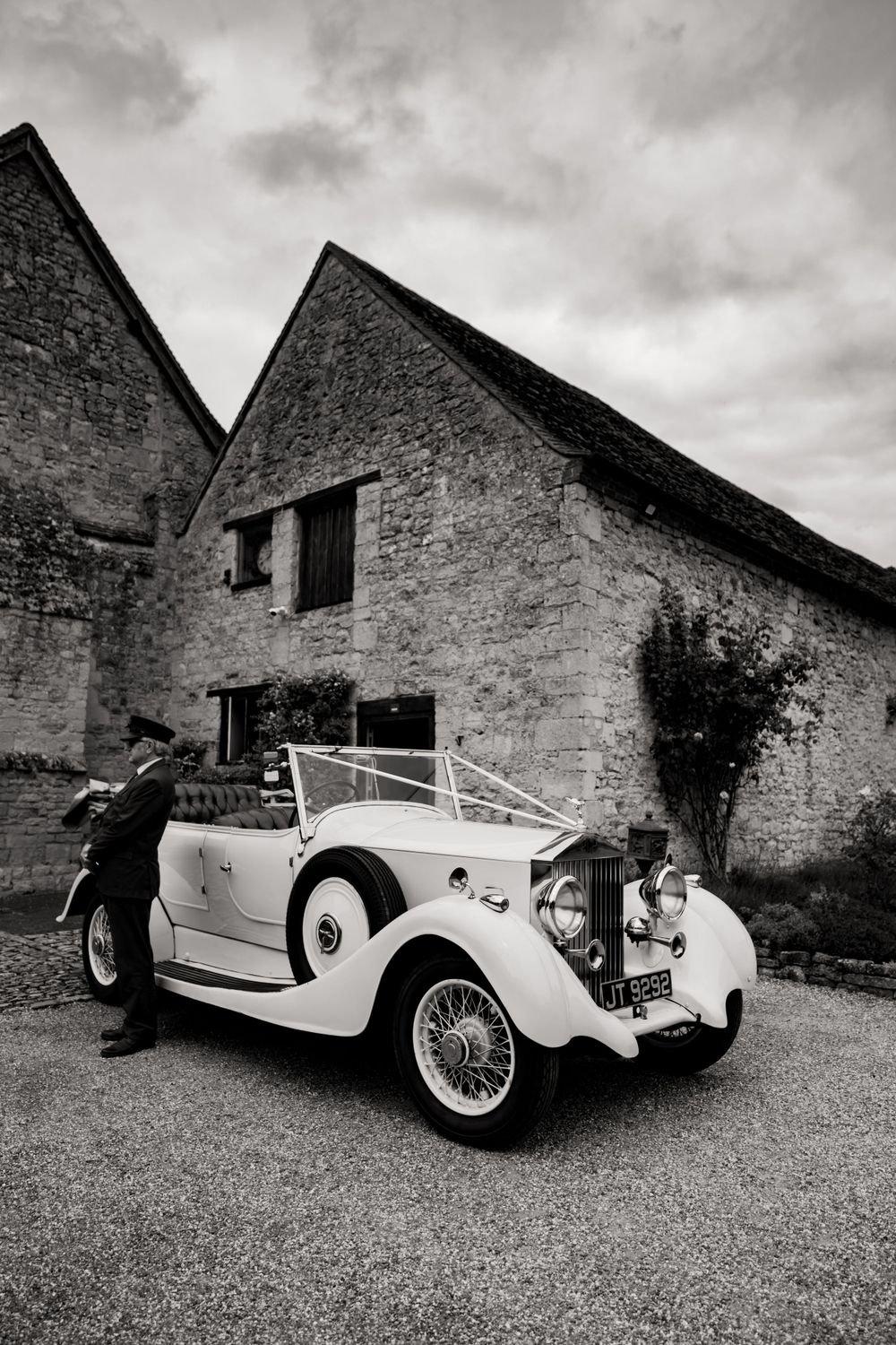 Vintage white luxury car parked outside rustic stone buildings in black and white photography.