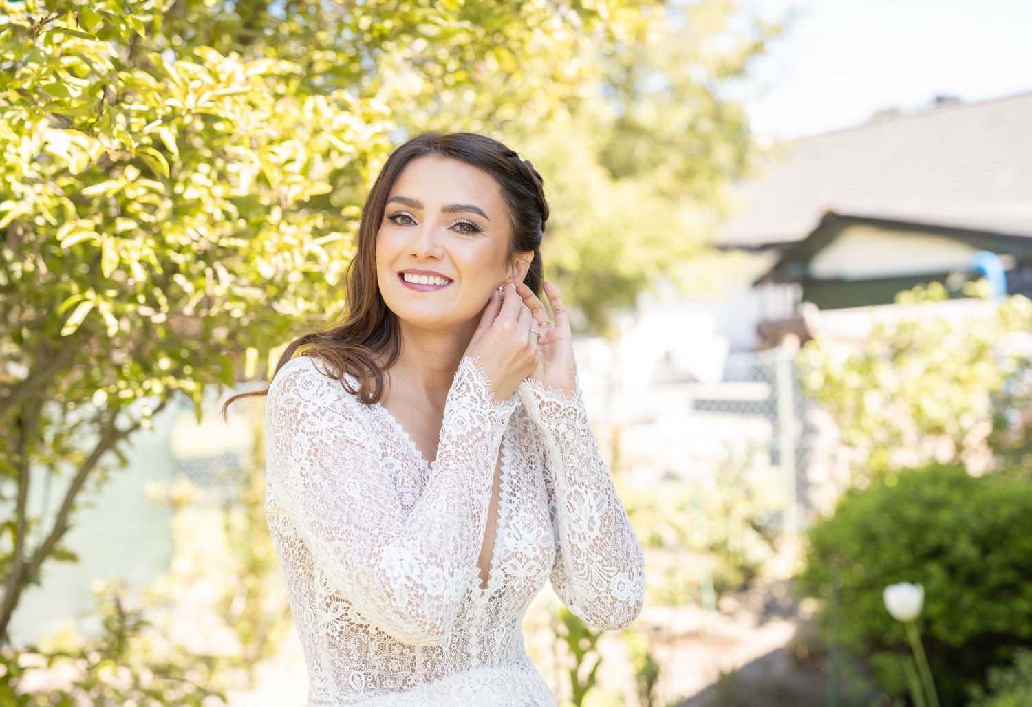 Ethereal bridal portrait in lace dress against sunny garden backdrop.