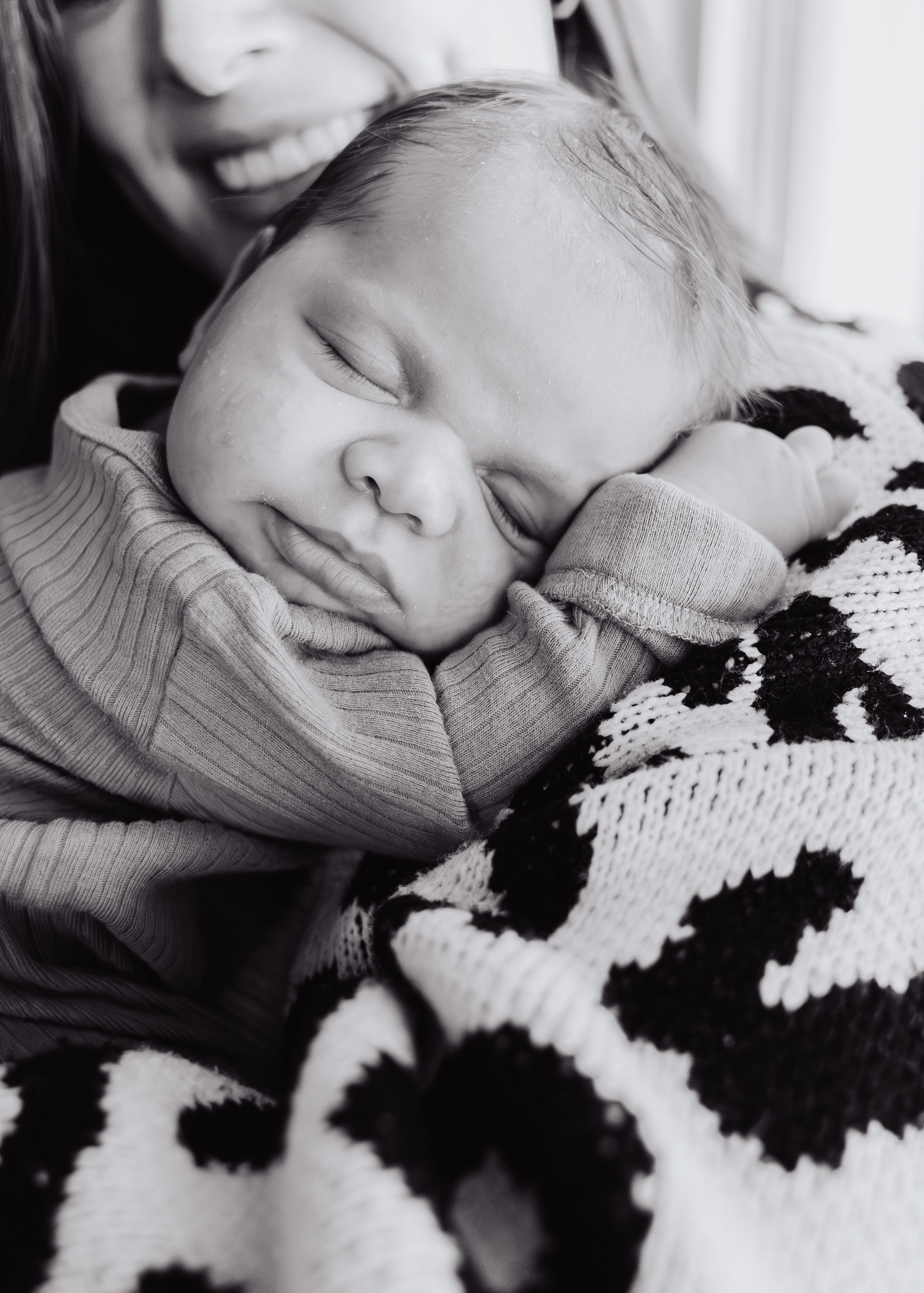 A sleeping baby in a gray outfit rests peacefully on a black and white patterned blanket.