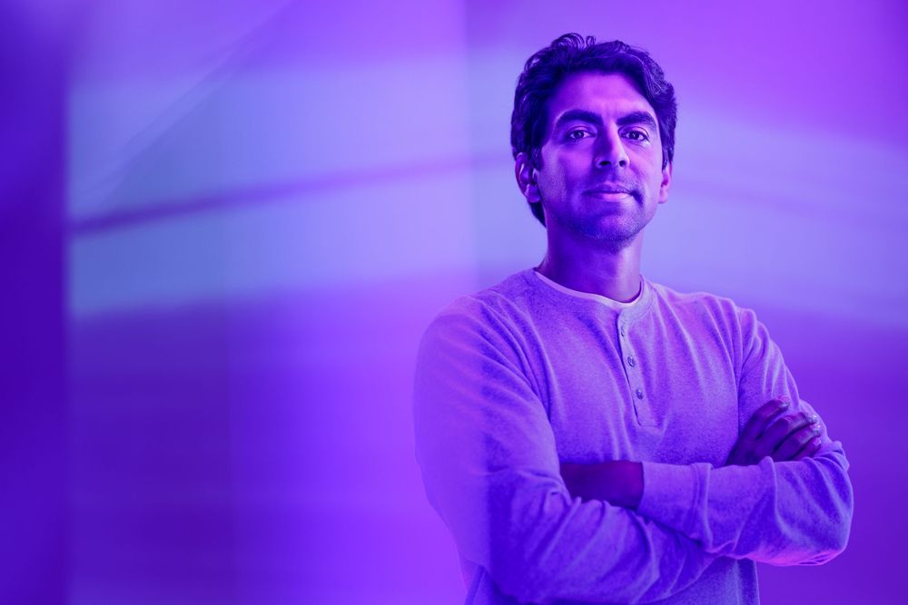 Professional portrait with crossed arms against purple atmospheric lighting.