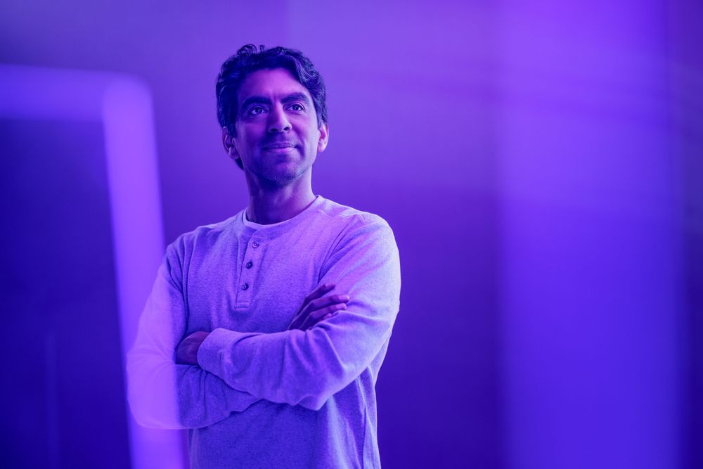 Portrait of person in light colored sweater against purple studio backdrop.