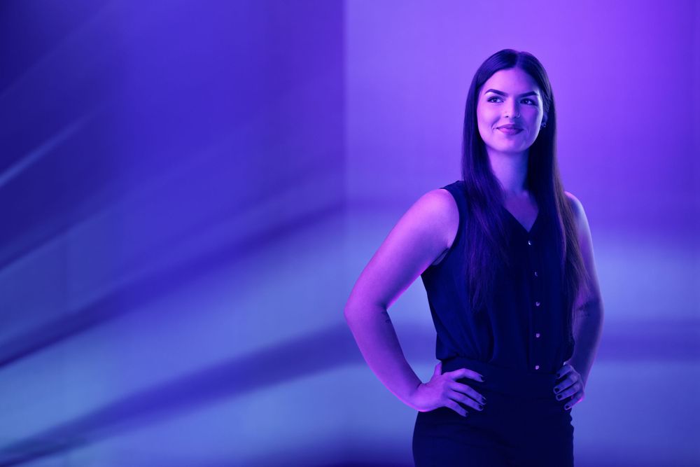 Woman in dark sleeveless top poses confidently against purple backdrop.