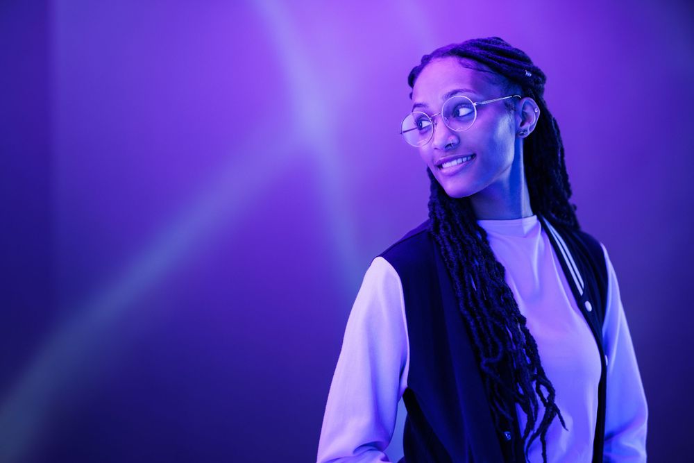 Portrait wearing glasses and light colored top against purple studio lighting.