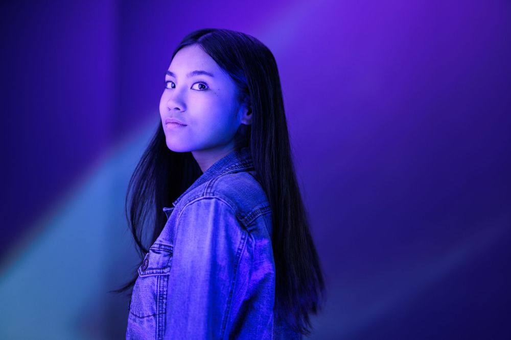 Figure in denim jacket poses against vibrant purple and blue lighting effects.