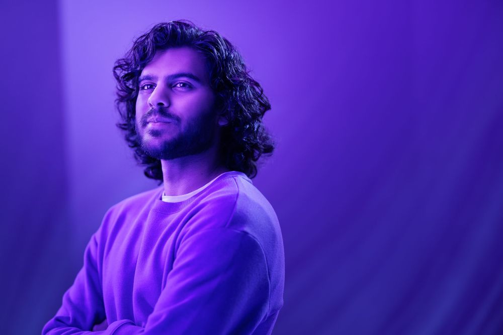 Person in purple sweatshirt with curly hair photographed in dramatic purple lighting.
