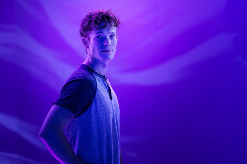 Person in casual attire poses against dramatic purple lighting effects.