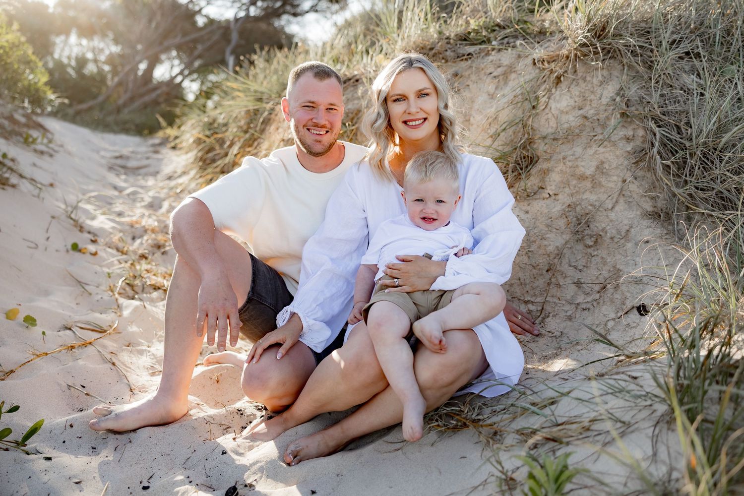 Family relaxing together on sandy beach slope during sunset photo session.
