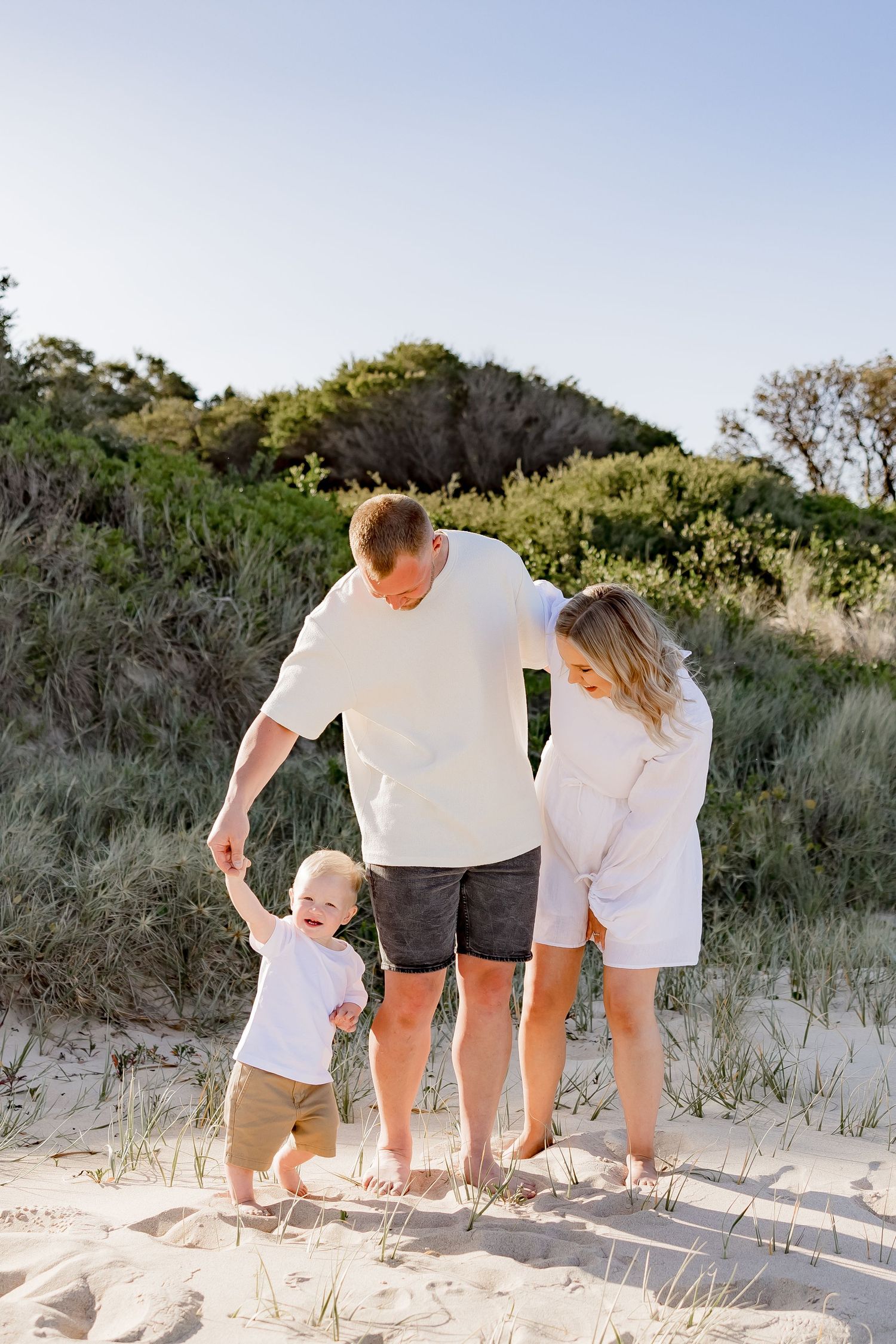Family standing together on sandy beach dunes during golden hour sunset photoshoot.