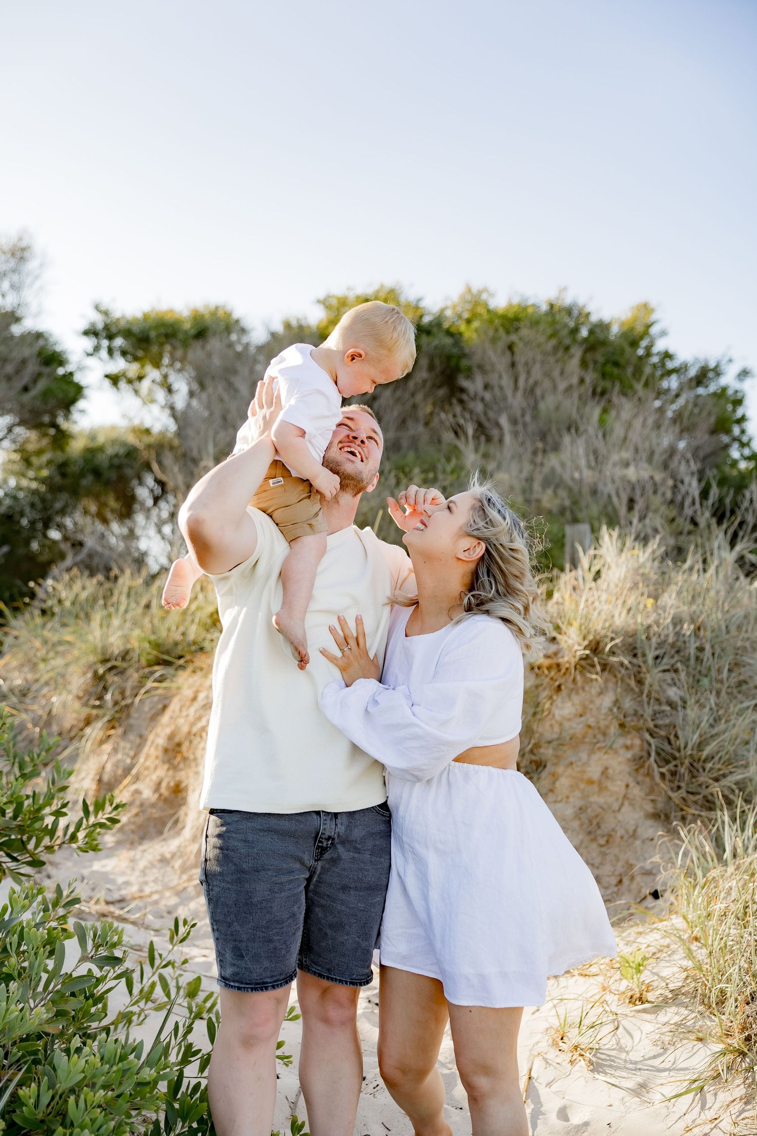 Playful family moment captured on sandy hillside during sunset.