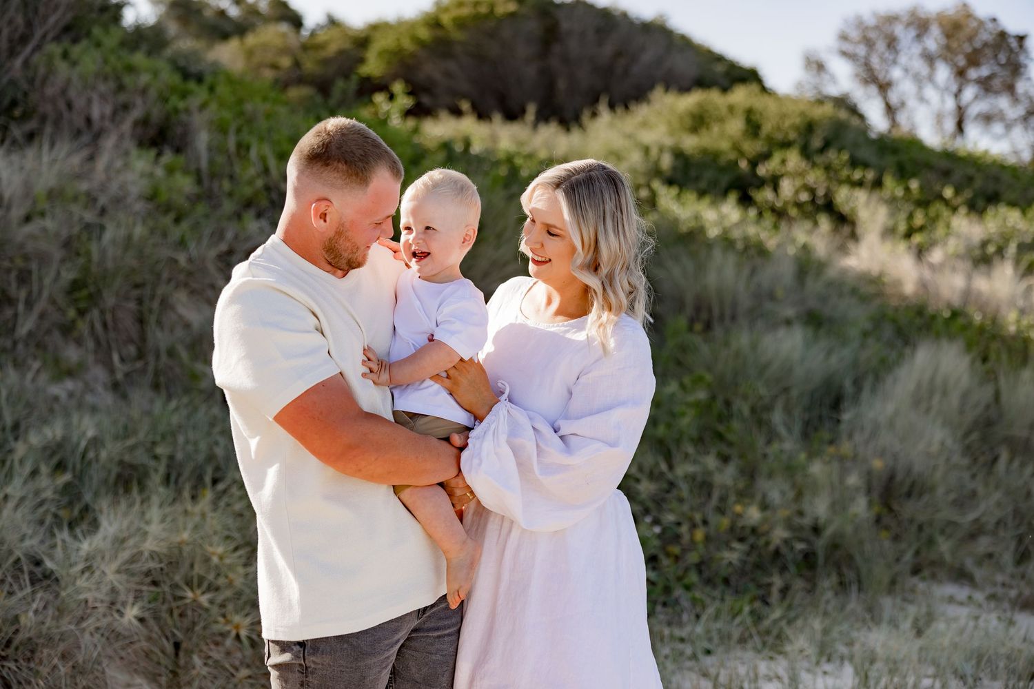 Parents embracing their young child on a sand dune during sunset.