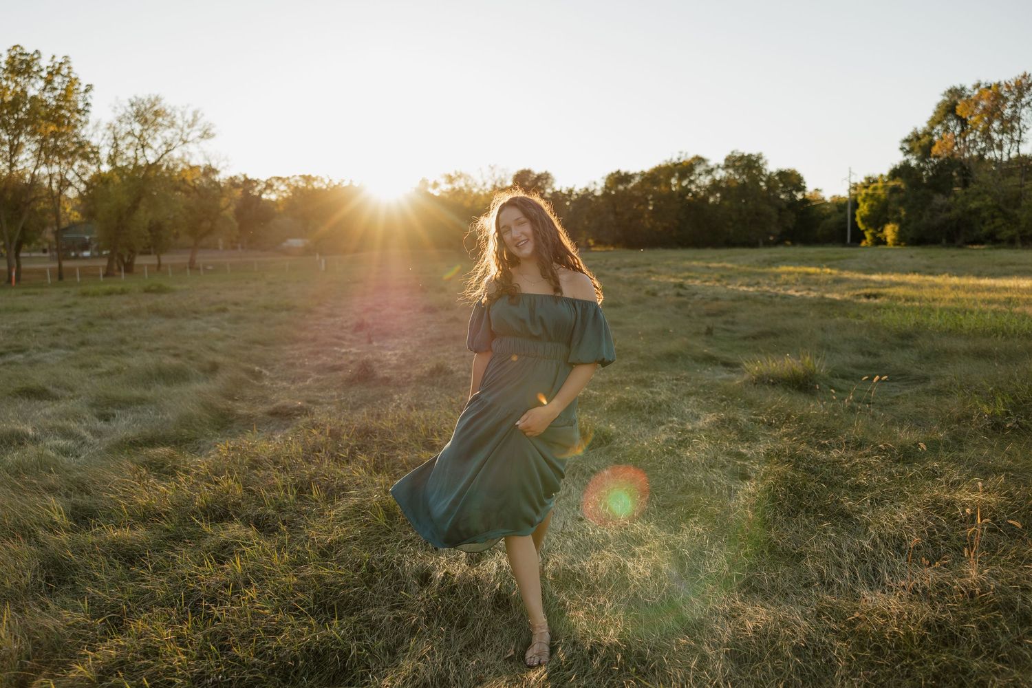 Person in flowing dress twirling in sunlit field during golden hour.