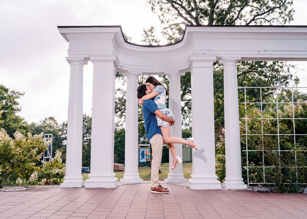 A romantic embrace under elegant white pillars in a garden setting.