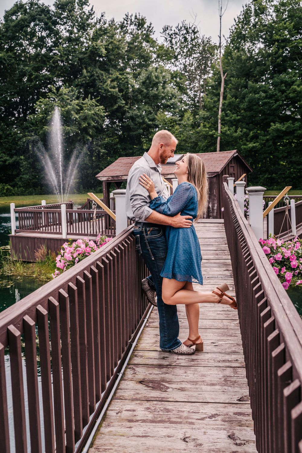 A romantic moment shared on a wooden bridge deck with a fountain and pink flowers in the background.