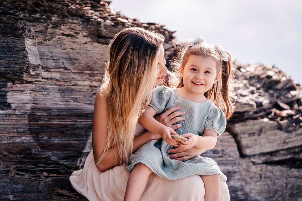 A tender moment between parent and child sitting together against rugged coastal rocks.