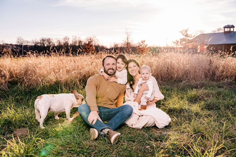 A family portrait in a golden field at sunset with their white dog.