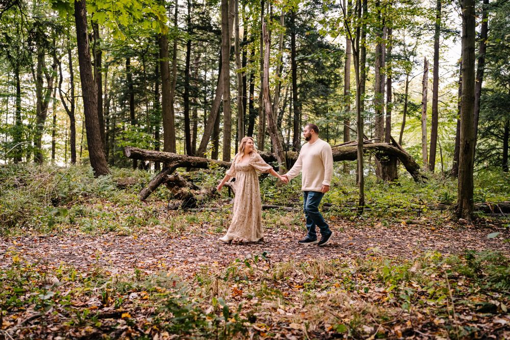 A couple sharing a romantic moment in a wooded area with fallen autumn leaves.