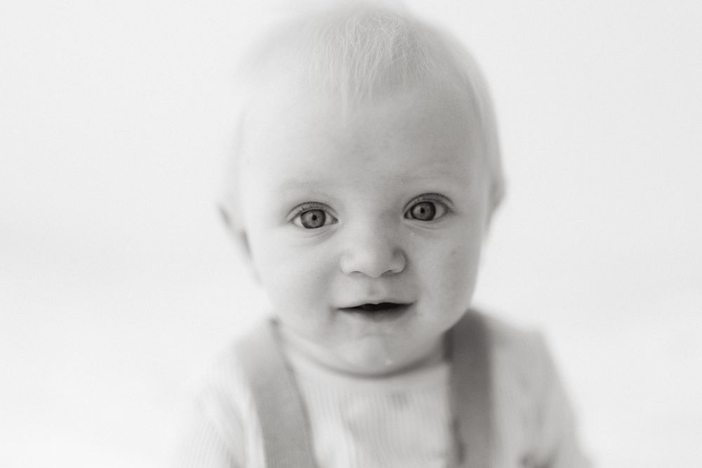Black and white portrait of a smiling baby with bright eyes against a light background.