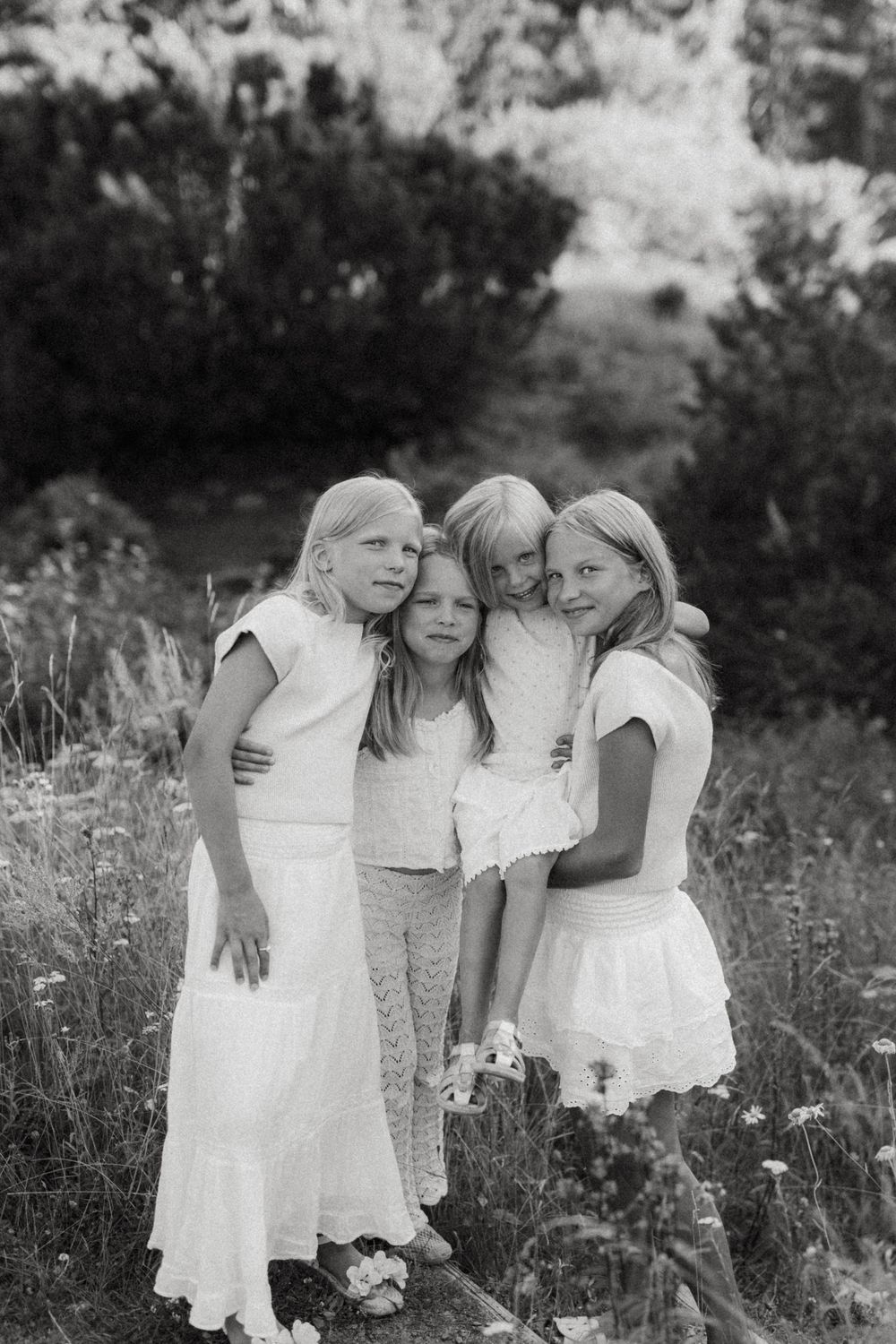 A series of black and white photographs showing children in white dresses standing together in a wildflower field.