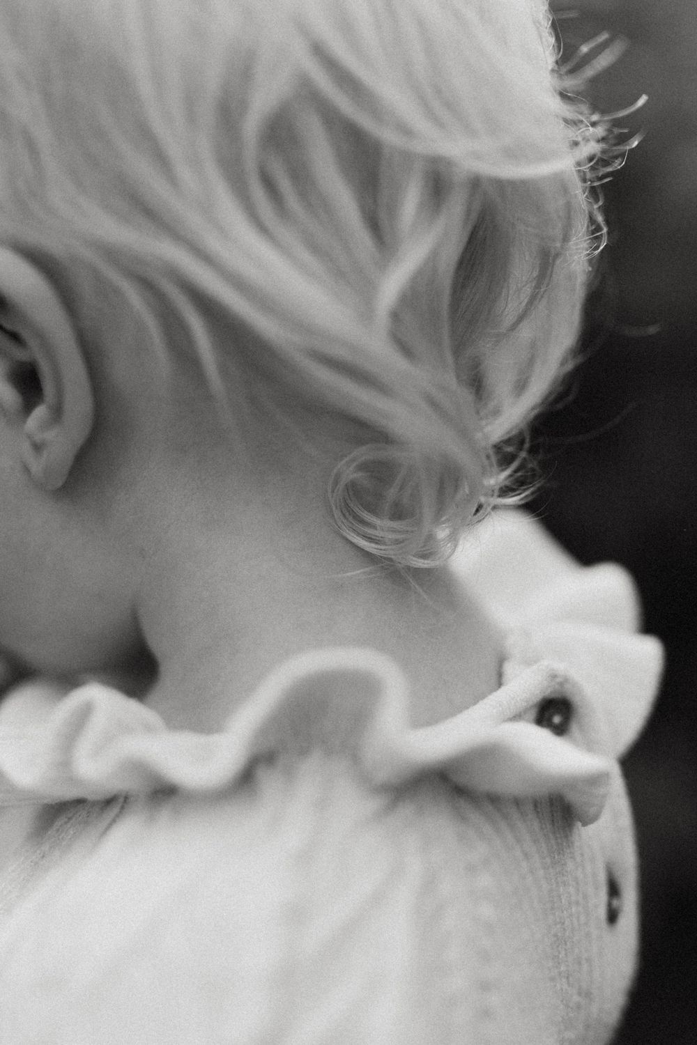 Black and white close-up photo of platinum blonde hair with soft wisps and curls against a dark background.