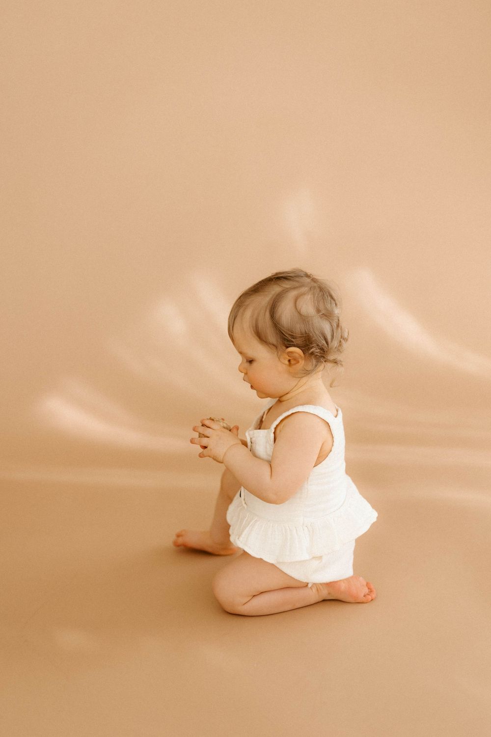 Five sequential photos show a baby in white clothing rolling over on a beige background in a studio setting.
