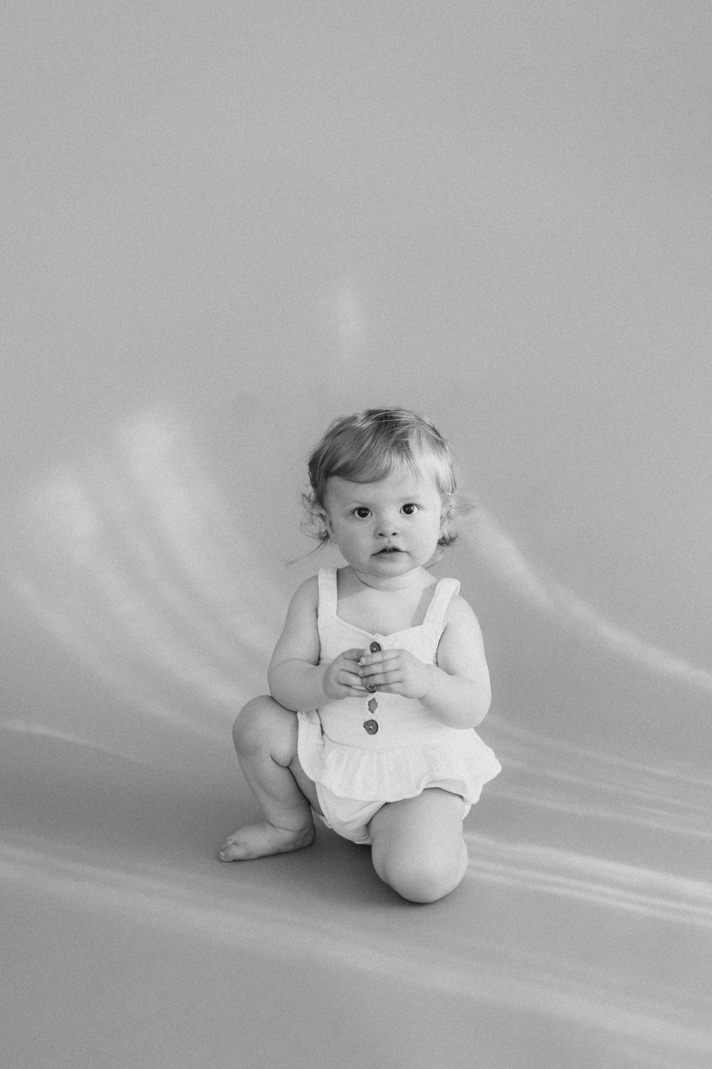 A series of black and white photos showing a baby in white clothing sitting and posing against a light background.