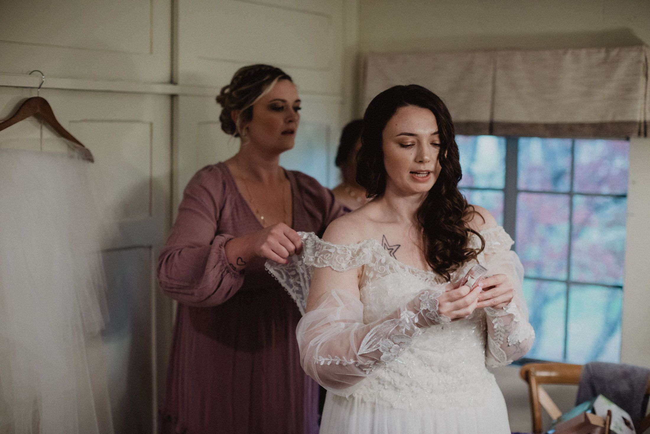 Bride getting final adjustments to her lace wedding gown in a sunlit dressing room.