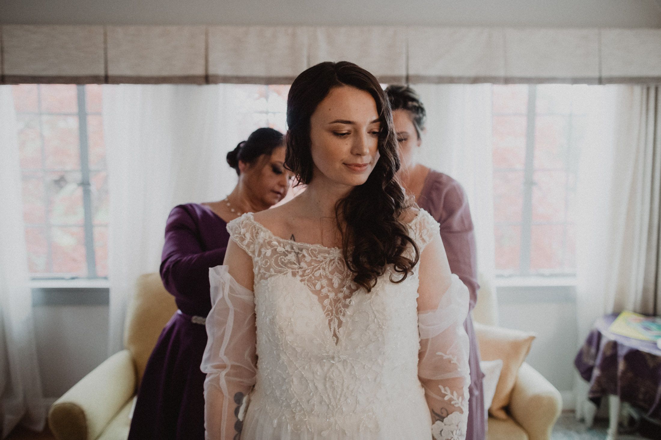 Delicate lace details of a wedding dress being adjusted in natural window light.