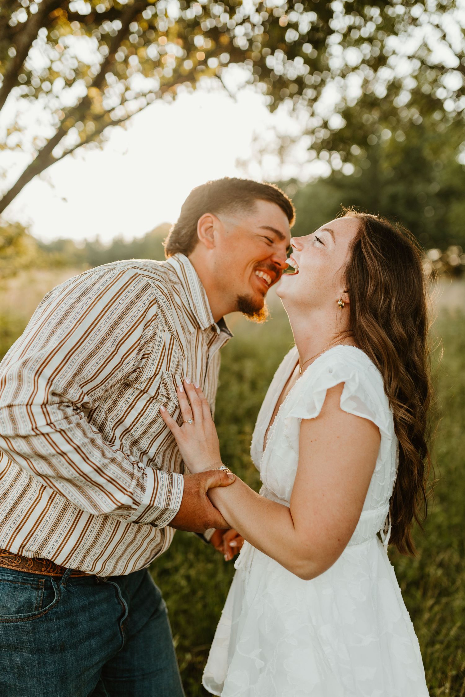 A couple shares a joyful moment together outdoors during a romantic photoshoot in natural sunlight.