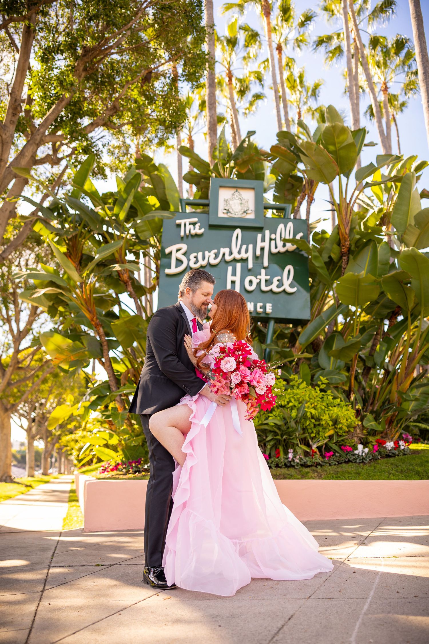 Romantic couple shares tender moments in front of the Beverly Hills Hotel sign surrounded by lush palm trees.