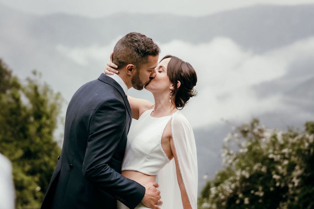 Newlyweds share an intimate kiss during their outdoor mountain wedding ceremony on an overcast day.