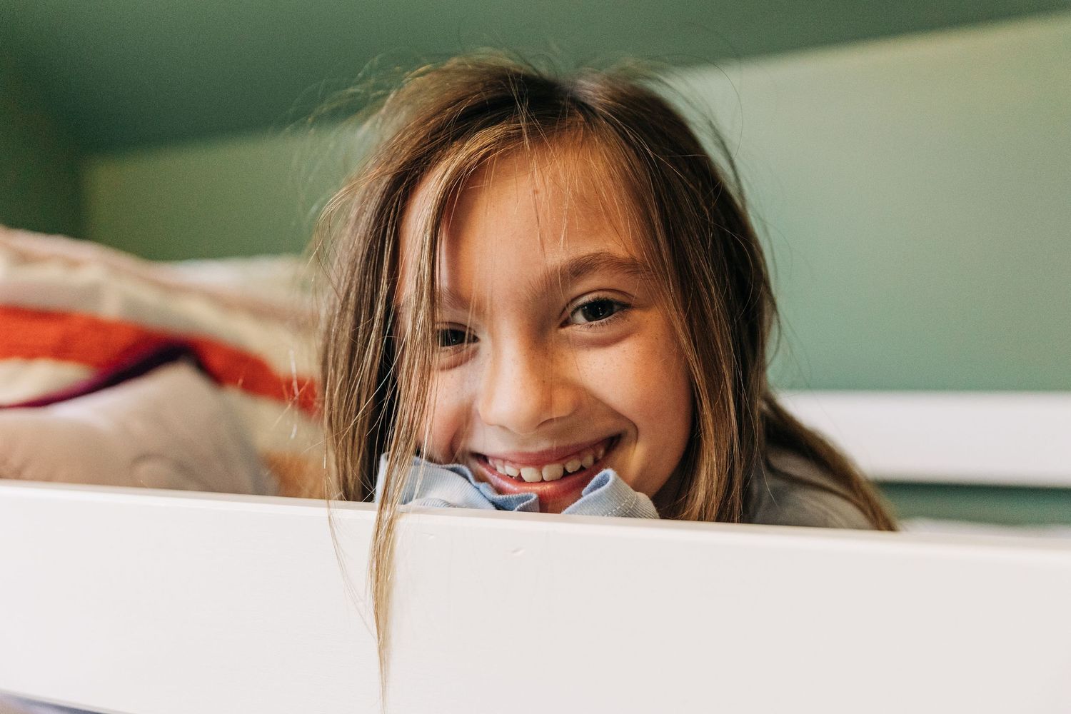 A young person peeks over a white surface with a bright, cheerful expression.