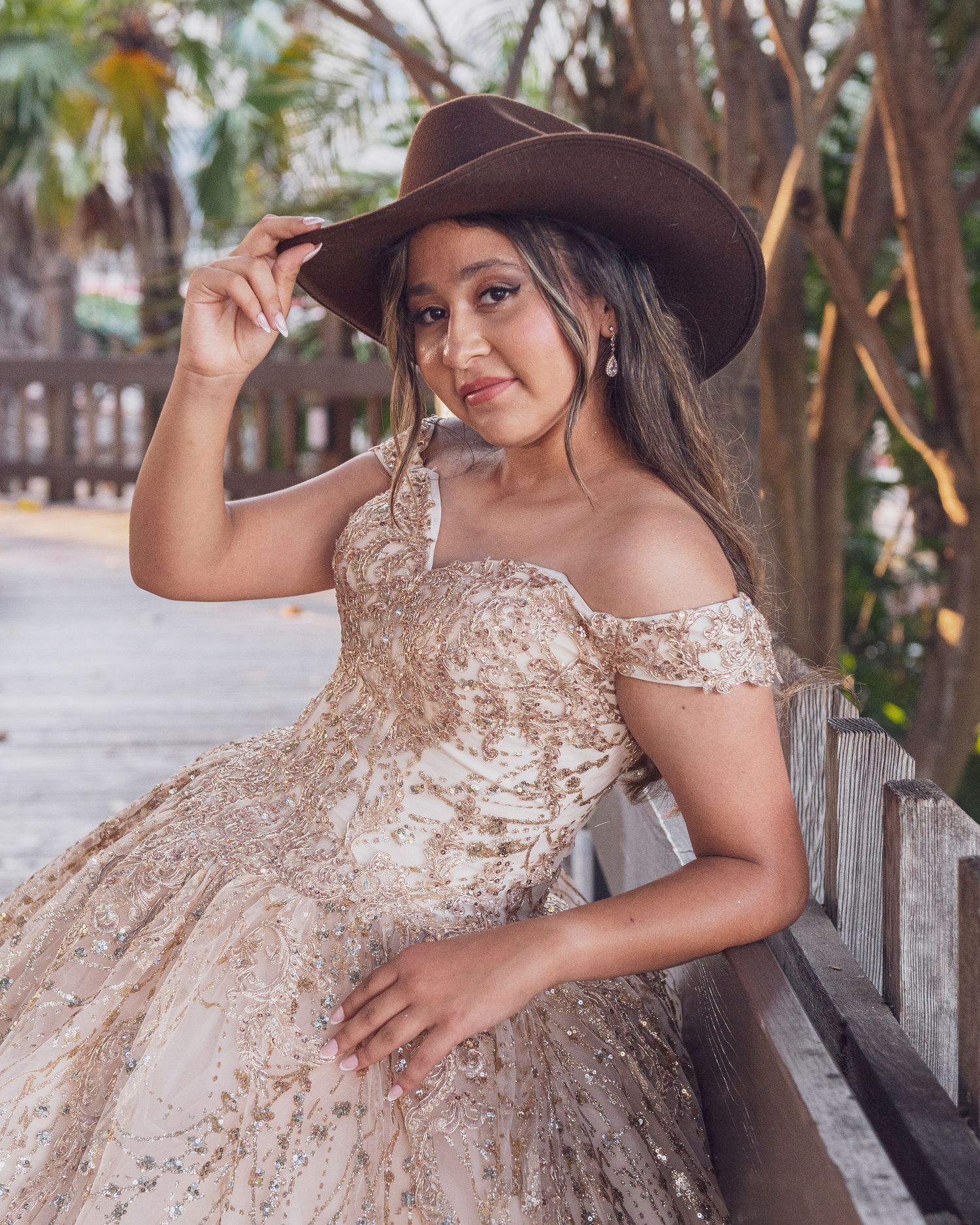 A sparkling champagne-colored quinceañera dress with intricate beading is showcased in an outdoor garden setting.