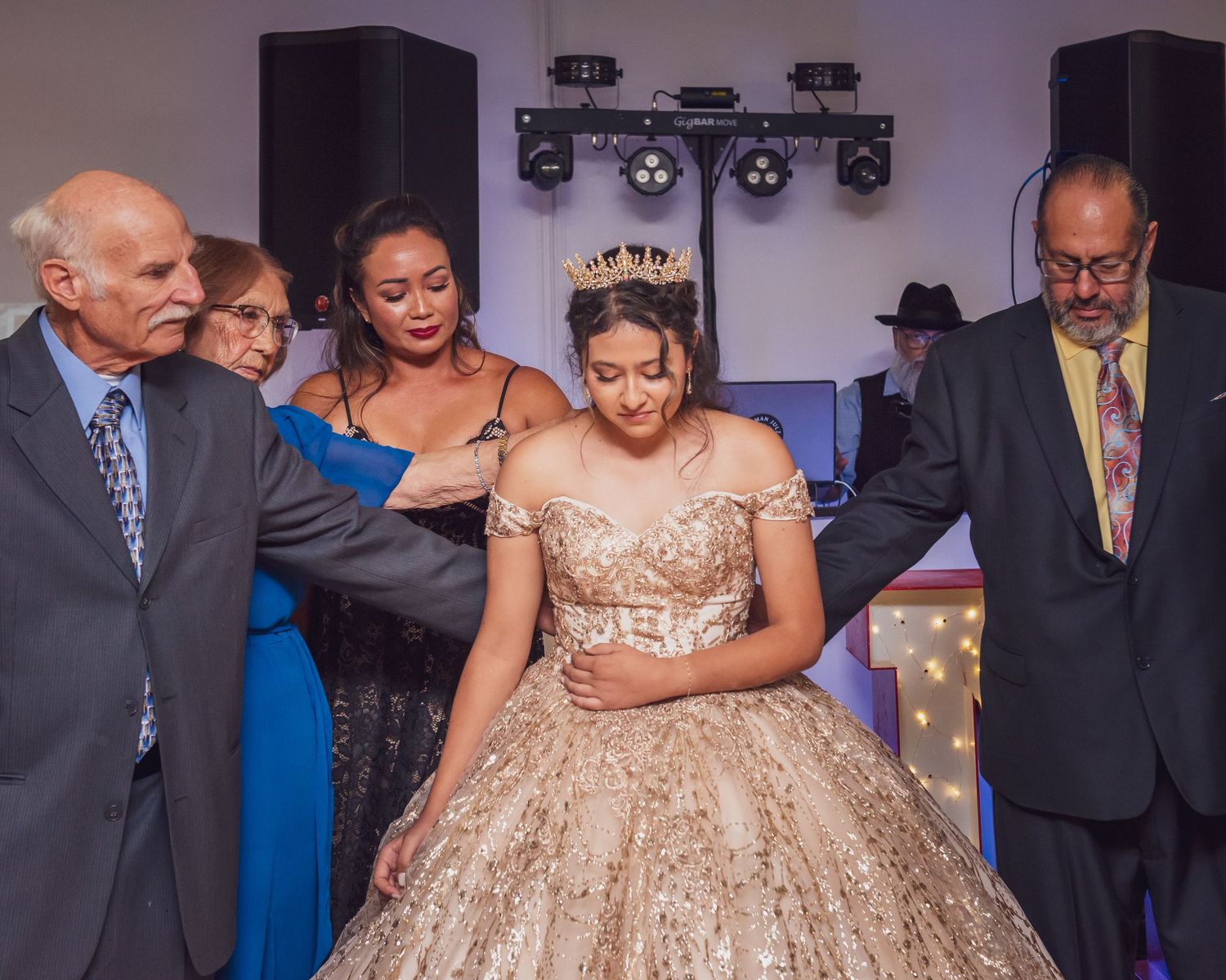 A celebration scene featuring a glittering gold ball gown surrounded by guests at an indoor venue.