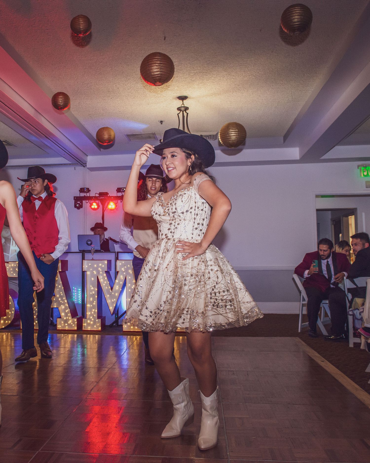 A quinceañera celebration features dancing on a wooden floor with red ambient lighting and paper lantern decorations.