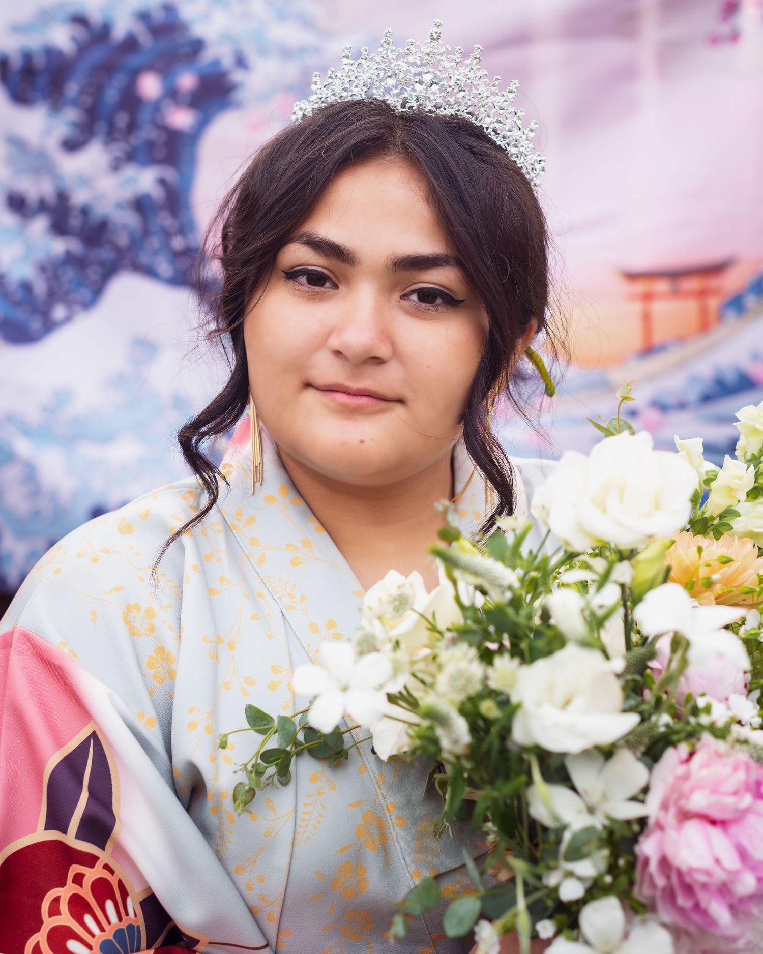 A person in a gray jacket holds a bouquet of fresh white and pink flowers against a blurred purple background.