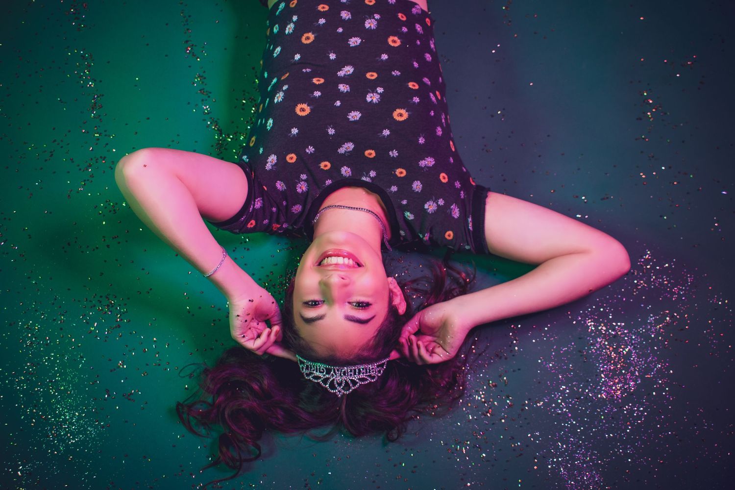 Artistic portrait of someone lying down with closed eyes against a dreamy teal and purple background with sparkles.