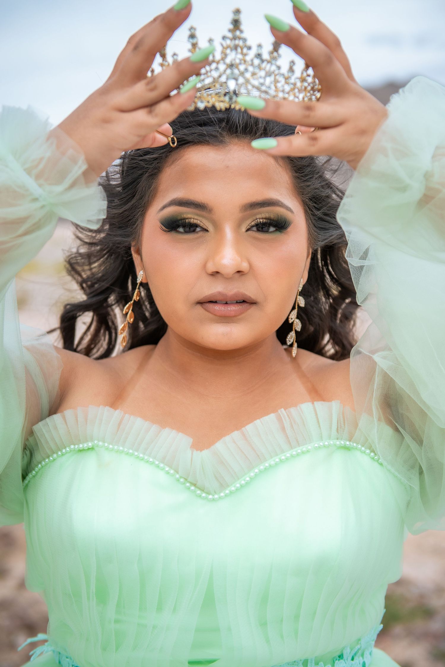 A person in a mint green tulle gown and crystal crown poses for a series of glamorous quinceañera portraits.