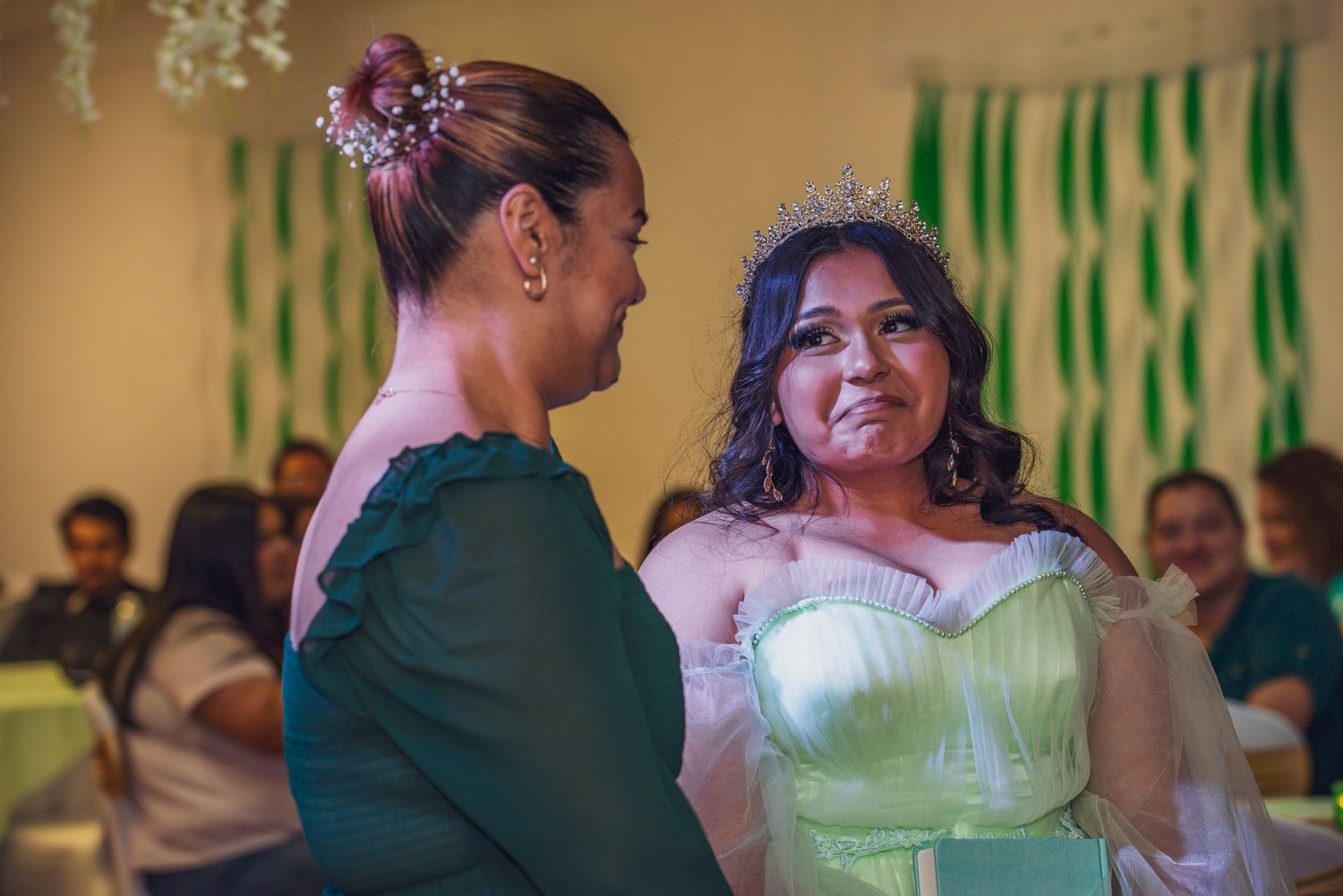 People dancing together at a celebration with green decorations visible in the background.