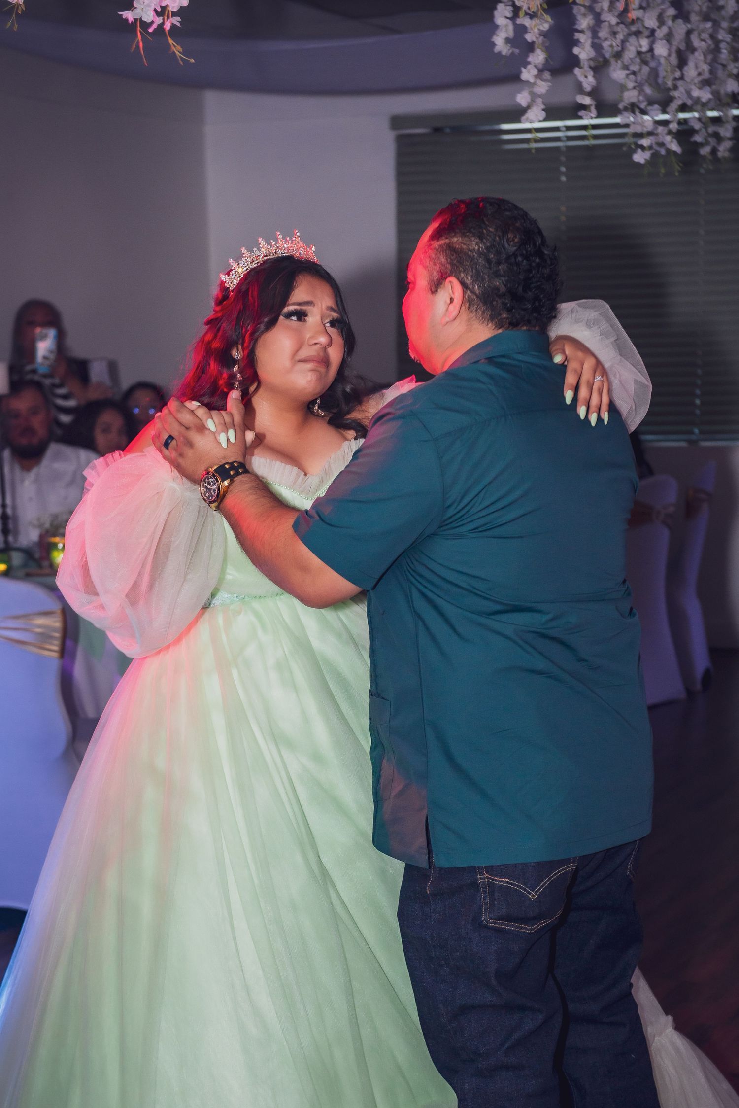 A couple dances together at a celebration while wearing a mint green gown and dark shirt under colorful lighting.