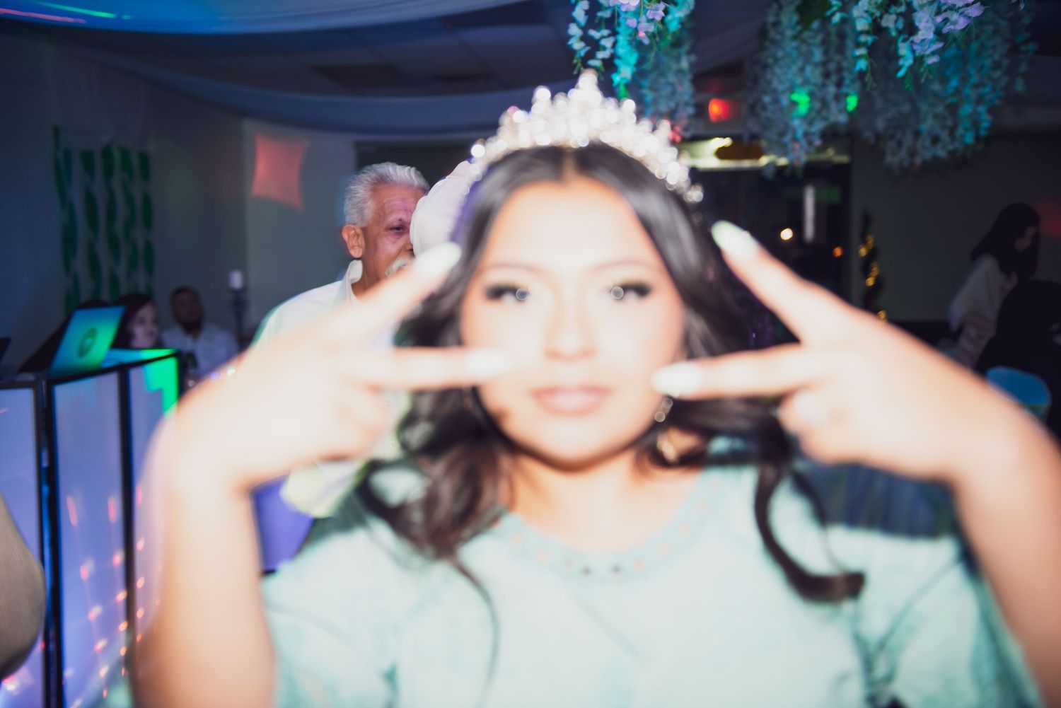 A person in a mint green dress dances and celebrates under blue party lighting at a festive event.