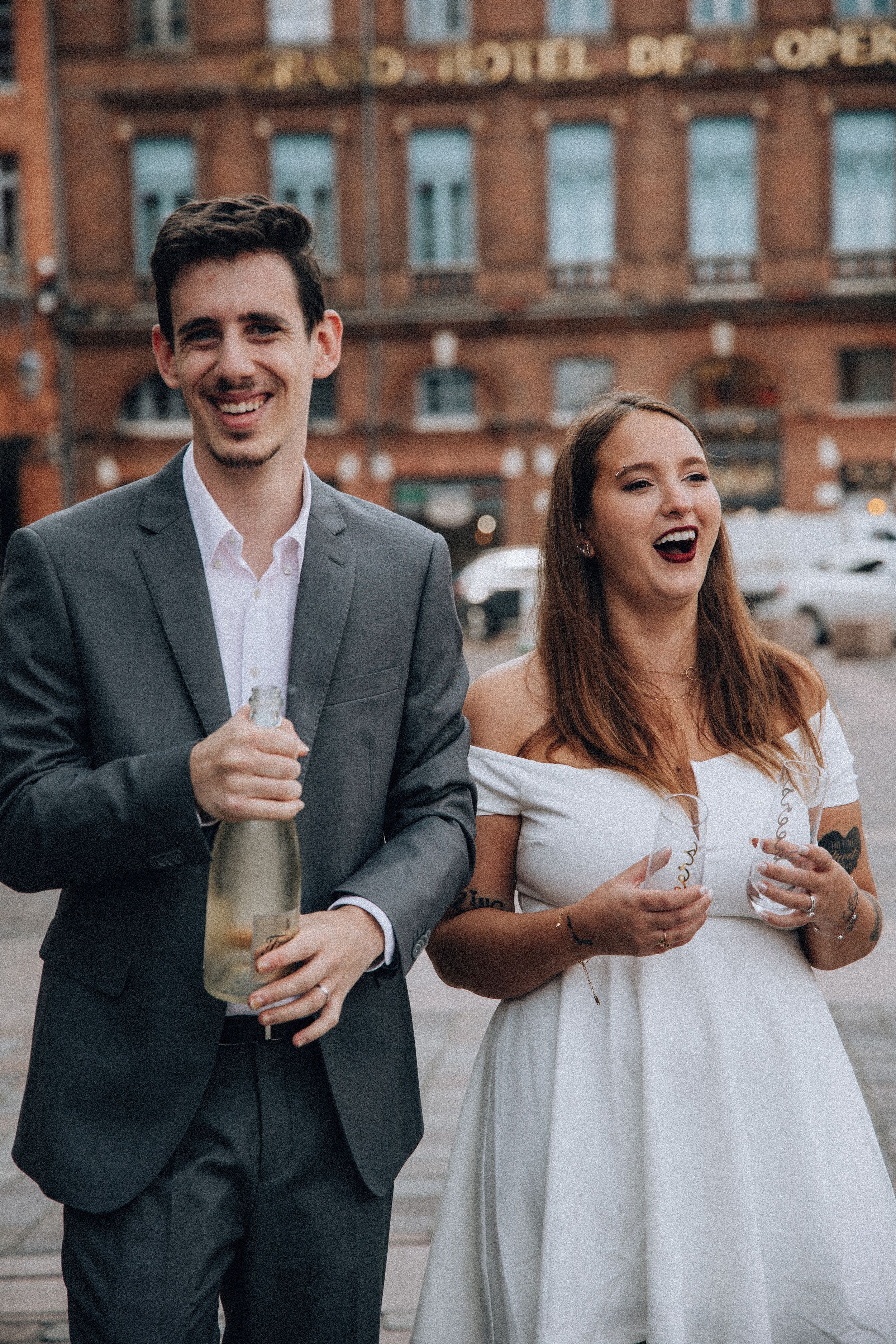 Happy couple celebrating wedding with champagne bottle outside Grand Hotel de l'Opera.